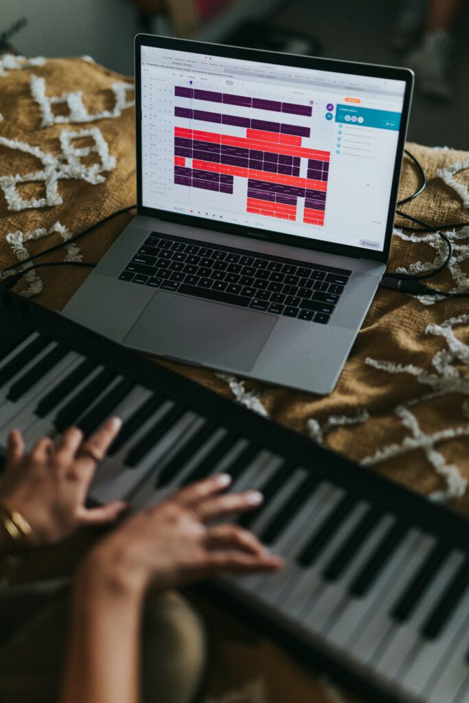 Junger man spielt E-Piano auf seinem Bett, mit einem offenen Laptop der ihm hilft